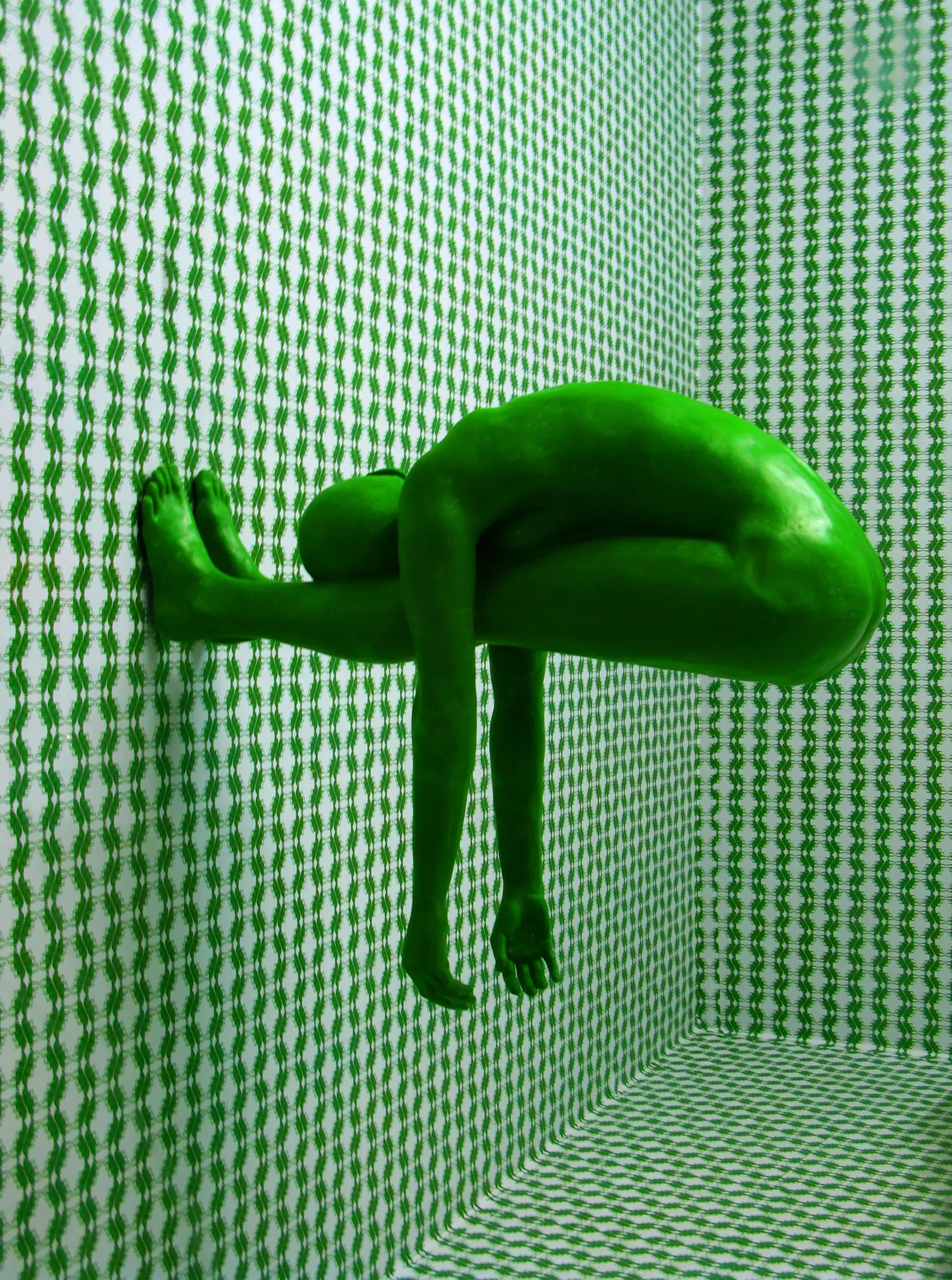 Bild von einem Mann komplett in Grün der mit den Füßen an einer Außenwand eines Zimmers steht.